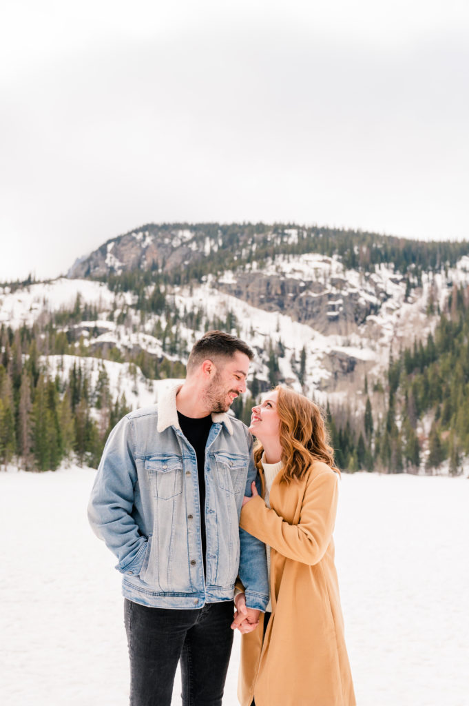 Casual Winter Mountain Engagement Outfit | Britni Girard Photography - Colorado Wedding Photography and Video Team | Camel Trench coats and jean jackets at Bear Lake in Rocky Mountain National Park | What to wear for an engagement session